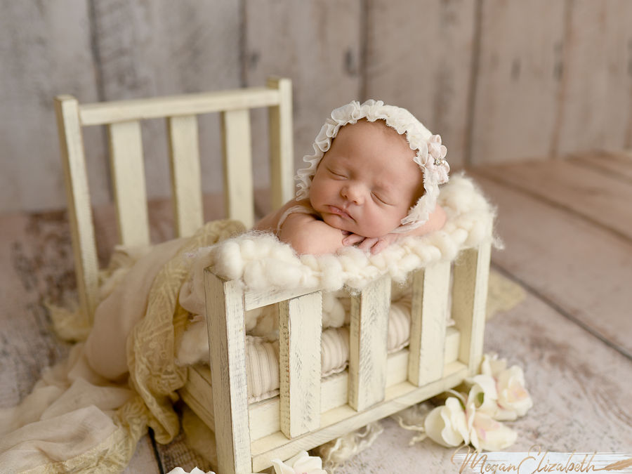 Sleeping newborn posed in a small cream bed