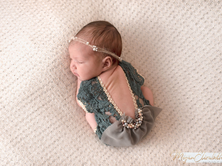 Sleeping newborn in a green lace outfit on a cream blanket