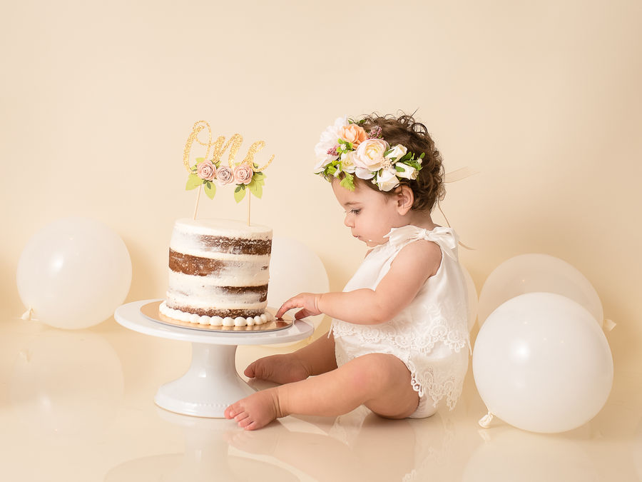 Baby beside a first birthday cake in a soft floral set
